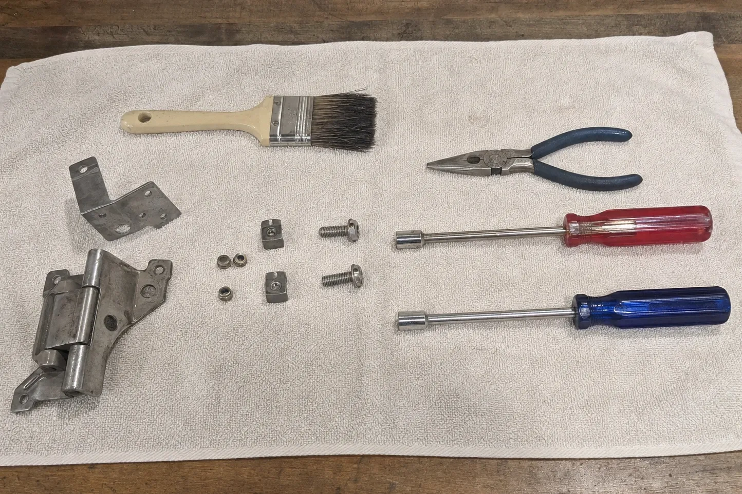 Oven door hinge with its spring barrel laid out beside brackets, clips, bolts and two nut drivers