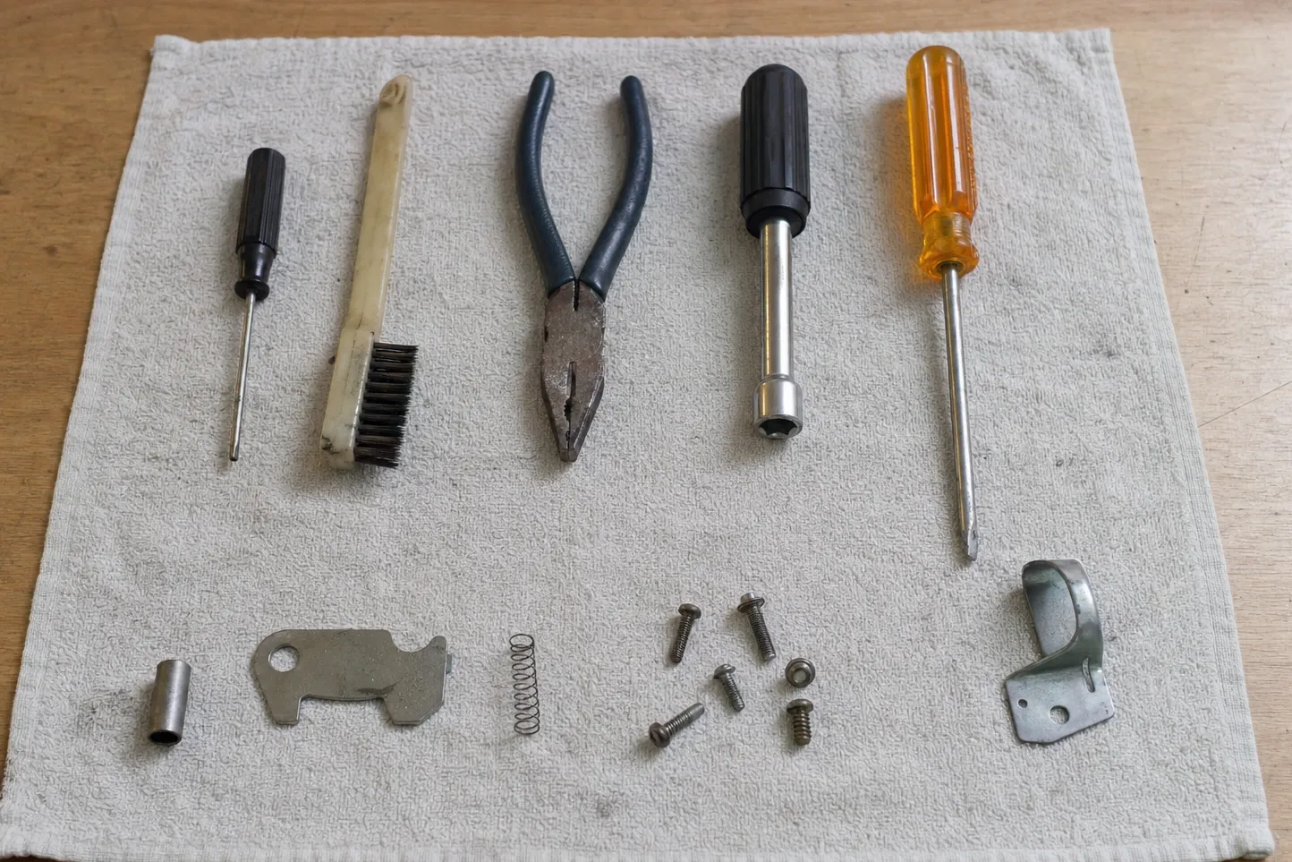 Latch cam, coil spring, sleeve and screws set out below a row of hand tools on a cloth